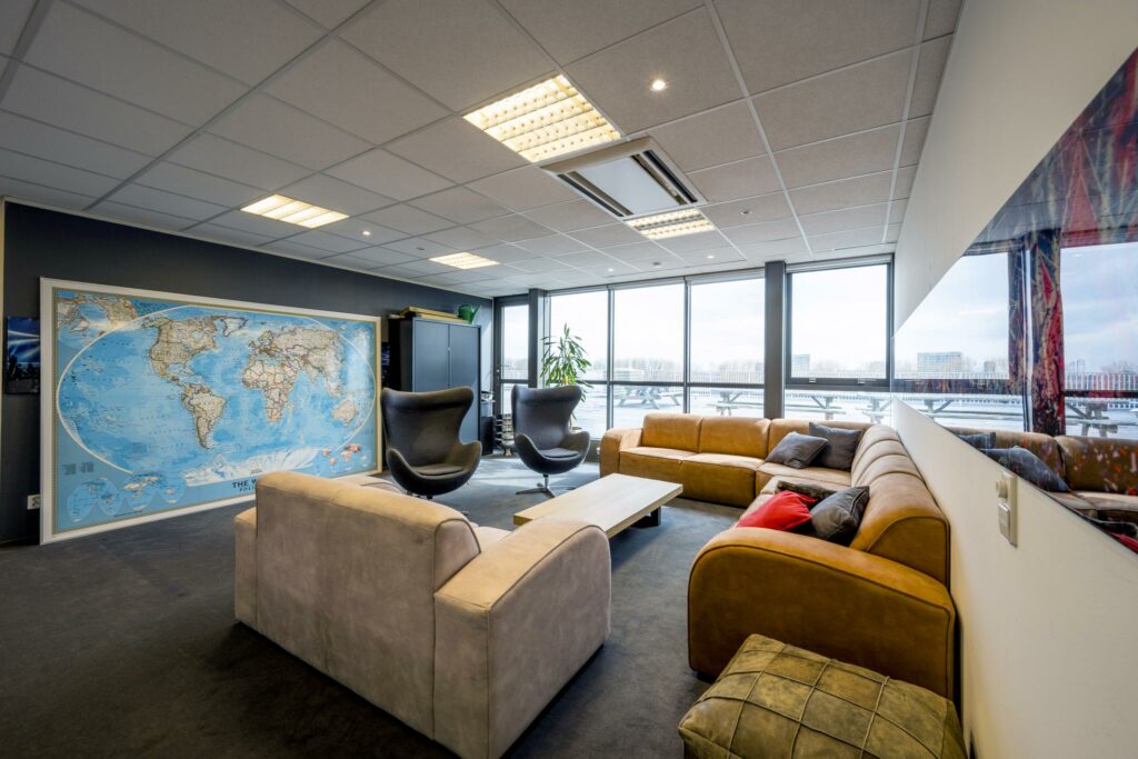 Een modern ingerichte lounge- of vergaderruimte aan de Anthony Fokkerweg met comfortabele banken, een wereldkaart aan de muur en grote ramen met uitzicht op een dakterras.